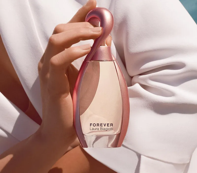 Una variante rosa del profumo "Forever", tenuto in mano da una figura femminile in abito bianco, che evoca eleganza e raffinatezza.